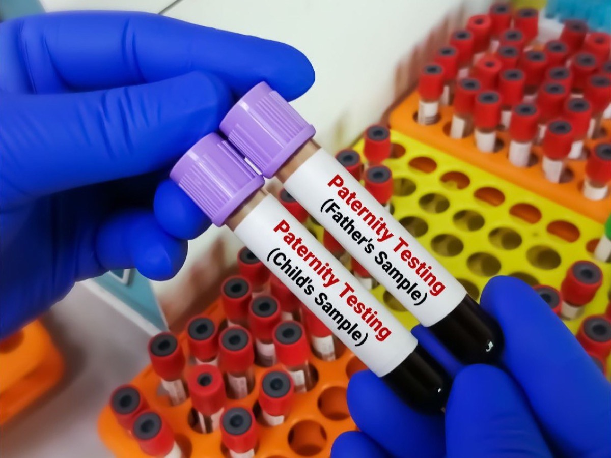 A gloved hand holding two labelled paternity testing sample tubes